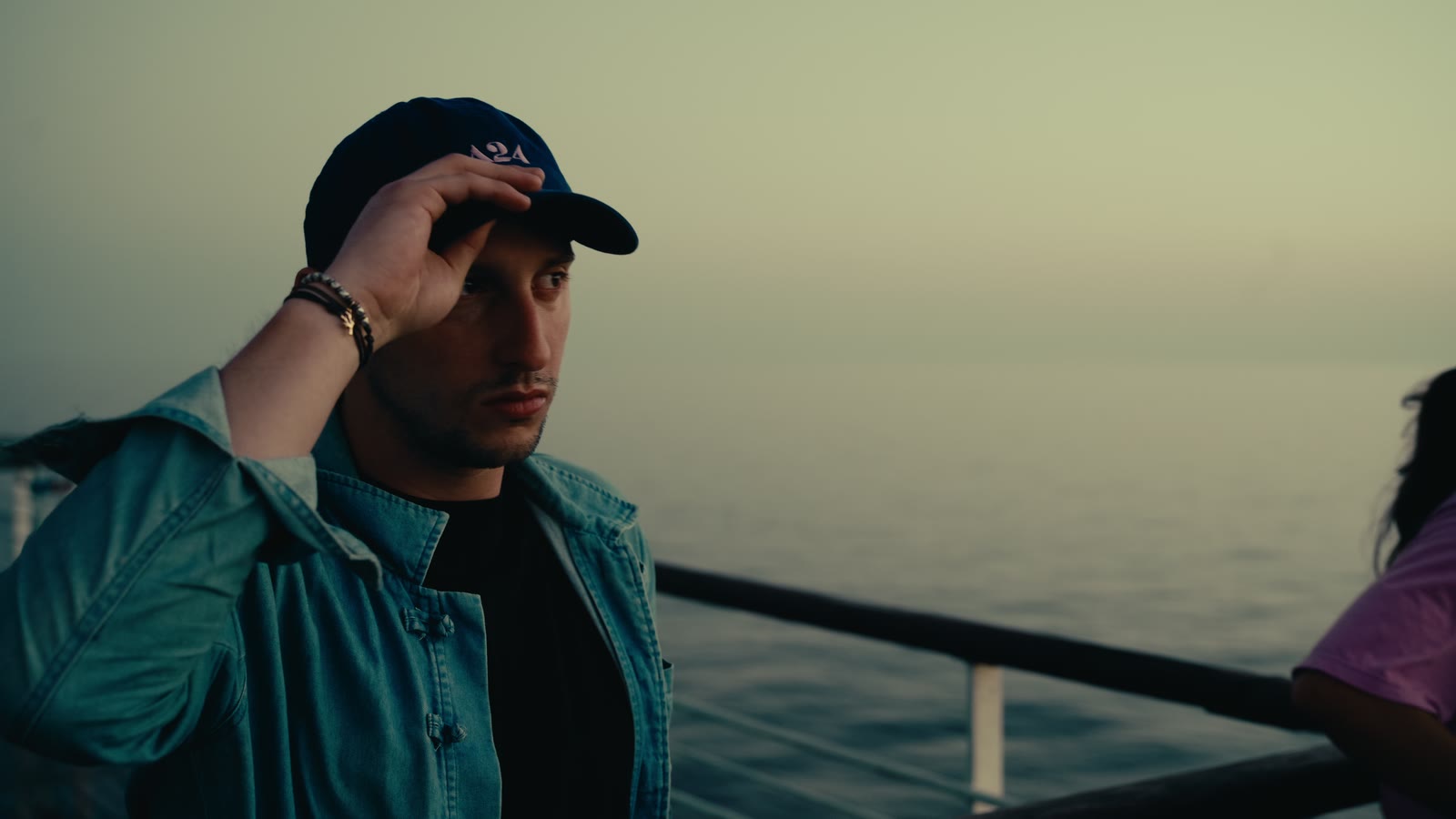 Maxime Silvy sur le pont d’un ferry, la main sur sa casquette, la mer au coucher du soleil.